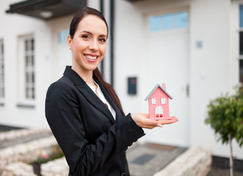 Real estate agent with model of house in front of home for sale, copy space